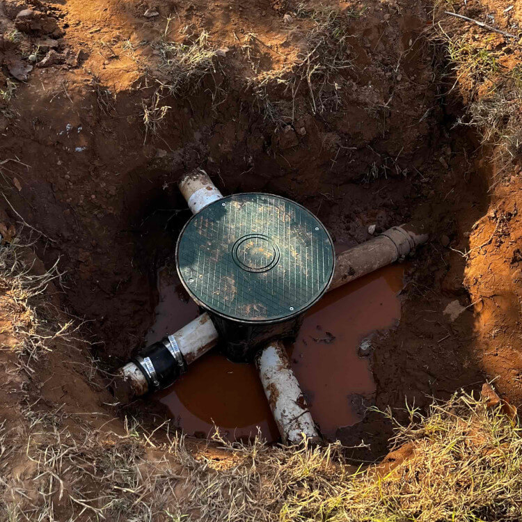 Drainage pipe with circular metal cover partially submerged in muddy ground