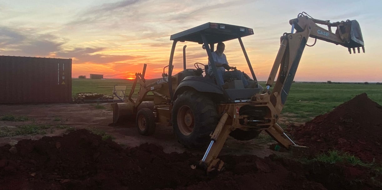 Backhoe excavator on dirt at sunset with dramatic orange sky