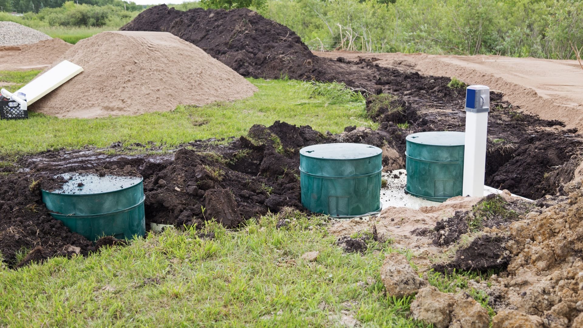 Green septic tanks installed in excavated ground with soil piles around