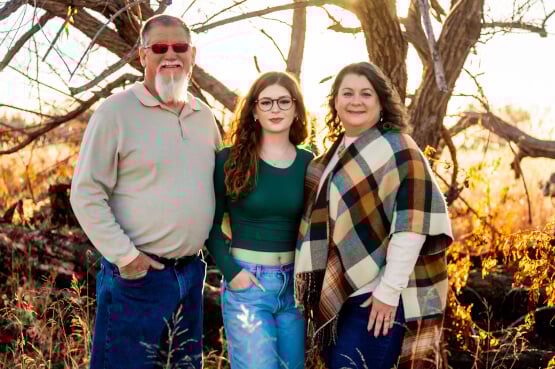Three family members pose together outdoors during golden autumn afternoon