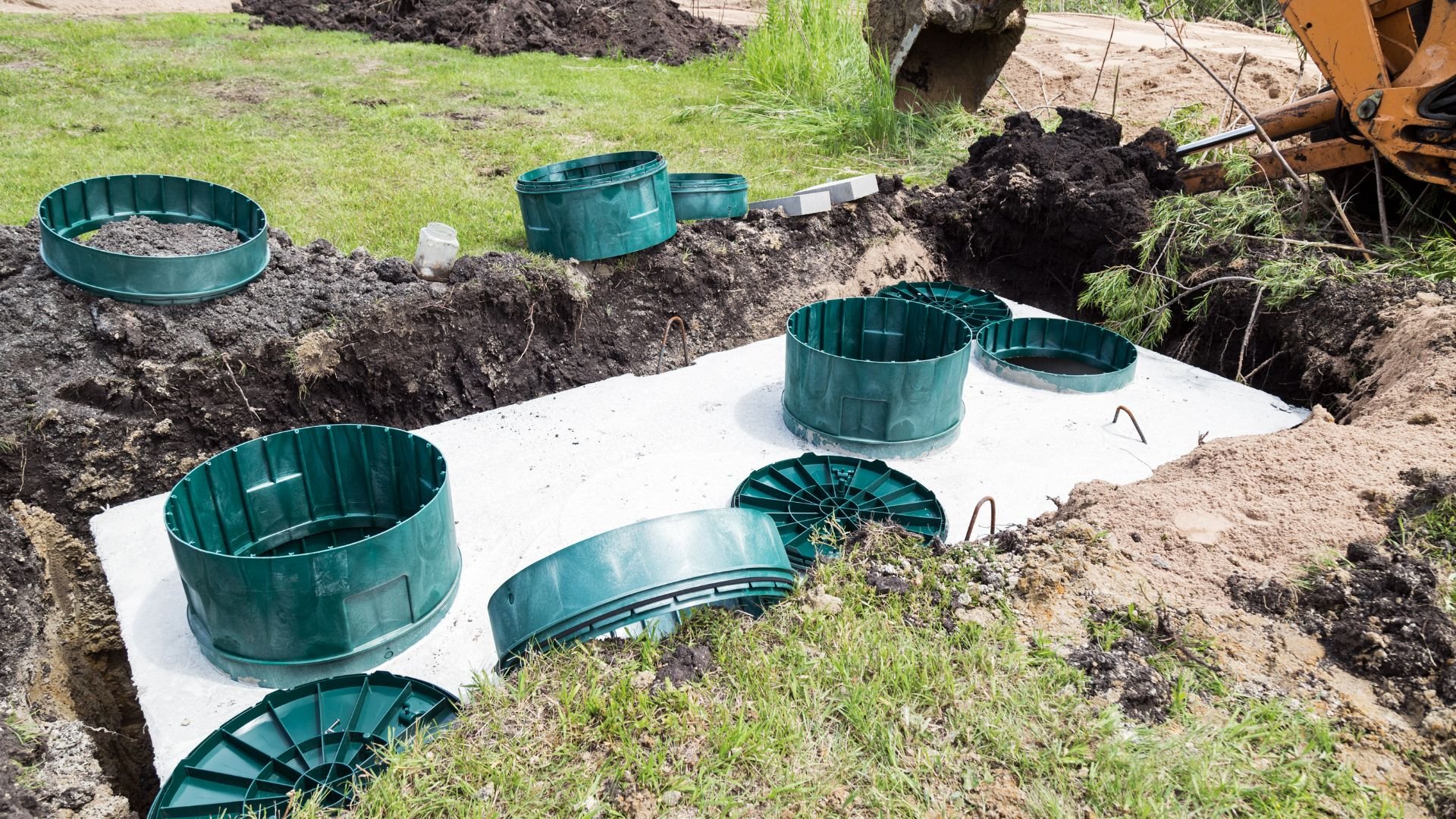 Green septic tank rings installed in excavated ground with construction equipment