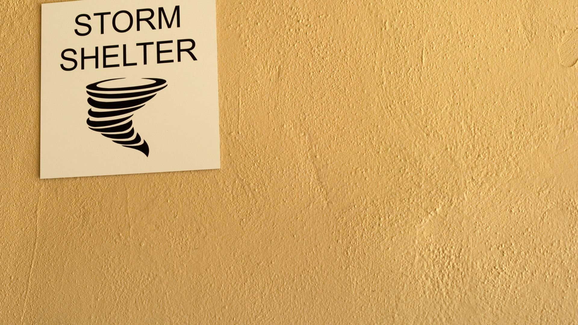 Storm shelter sign with tornado icon on textured yellow wall